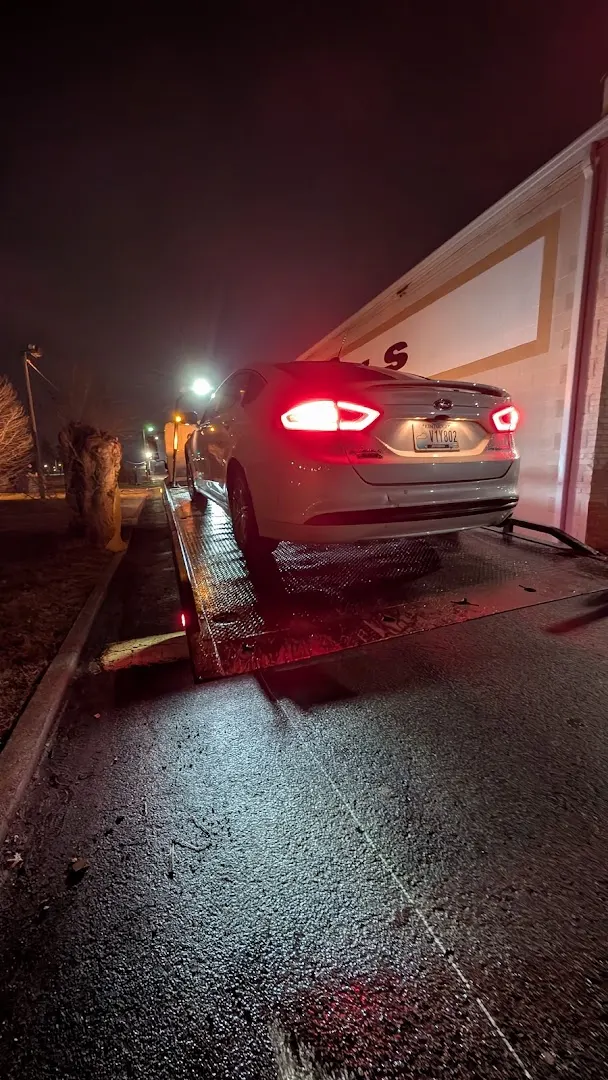 Rear view of a white sedan on the flatbed at night, tail lights on.