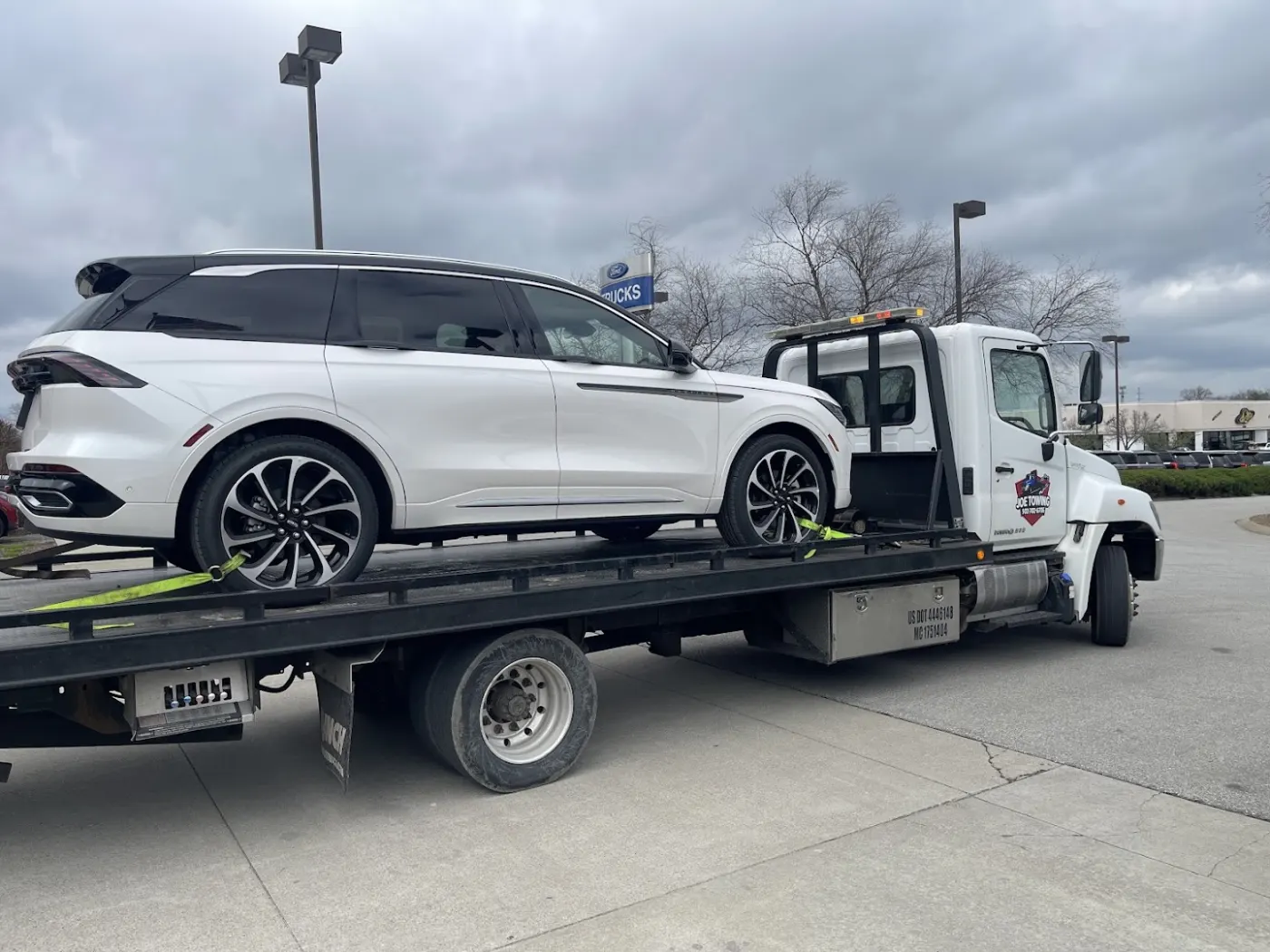 Joe Towing flatbed truck carrying a white SUV in daylight.